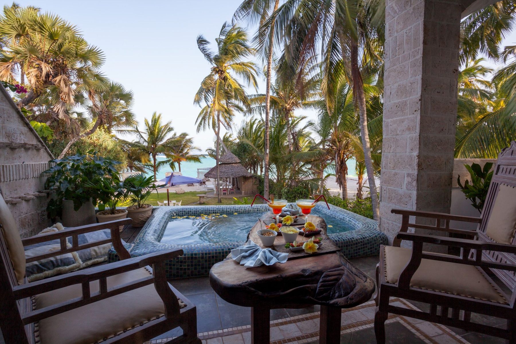 Private terrace of the Jacuzzi Suite at The Maji, with a hot tub, armchairs and palms leading to the beach