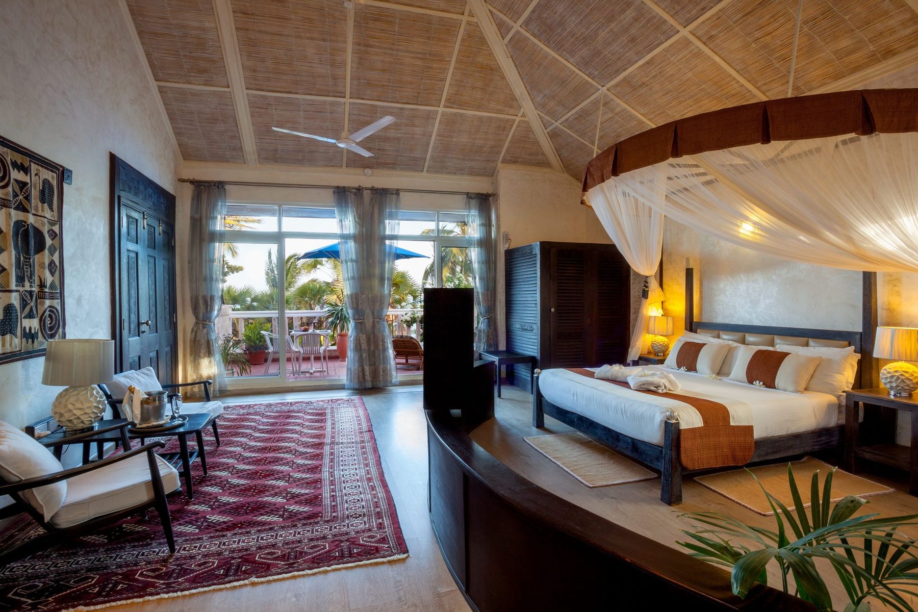 Ocean suite at The Maji with a canopy bed, a red rug and glass doors open to a terrace and the sea