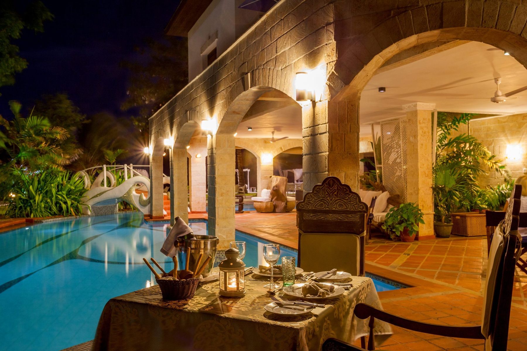 A table set for dinner beside the lit pool under stone arches at The Maji at night