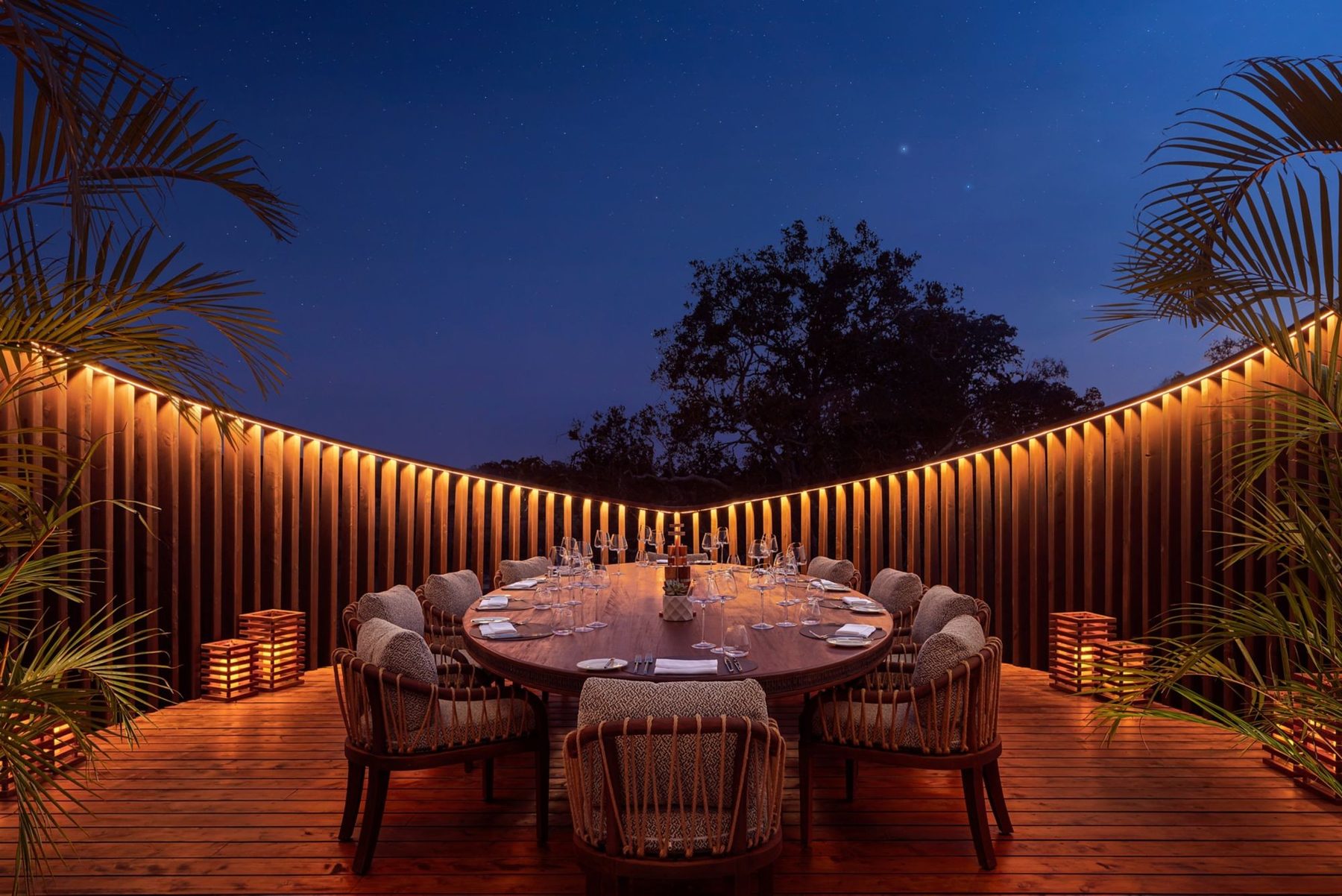 Round dinner table on a lantern-lit wooden deck at The Ritz-Carlton, Masai Mara Safari Camp at dusk