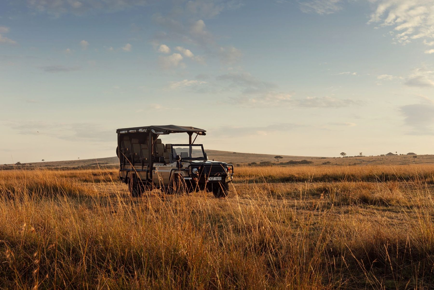 Open game drive vehicle crossing golden grassland on the Mara plains near The Ritz-Carlton, Masai Mara Safari Camp