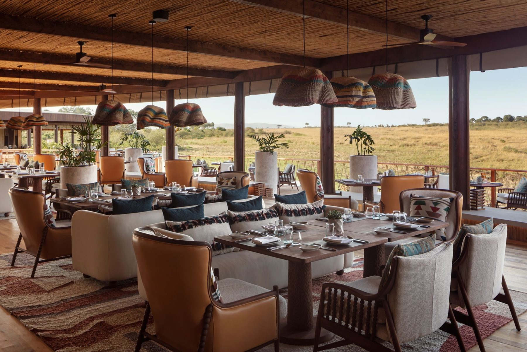 Open-sided restaurant at The Ritz-Carlton, Masai Mara Safari Camp with armchairs, woven pendant lamps and views over the plains