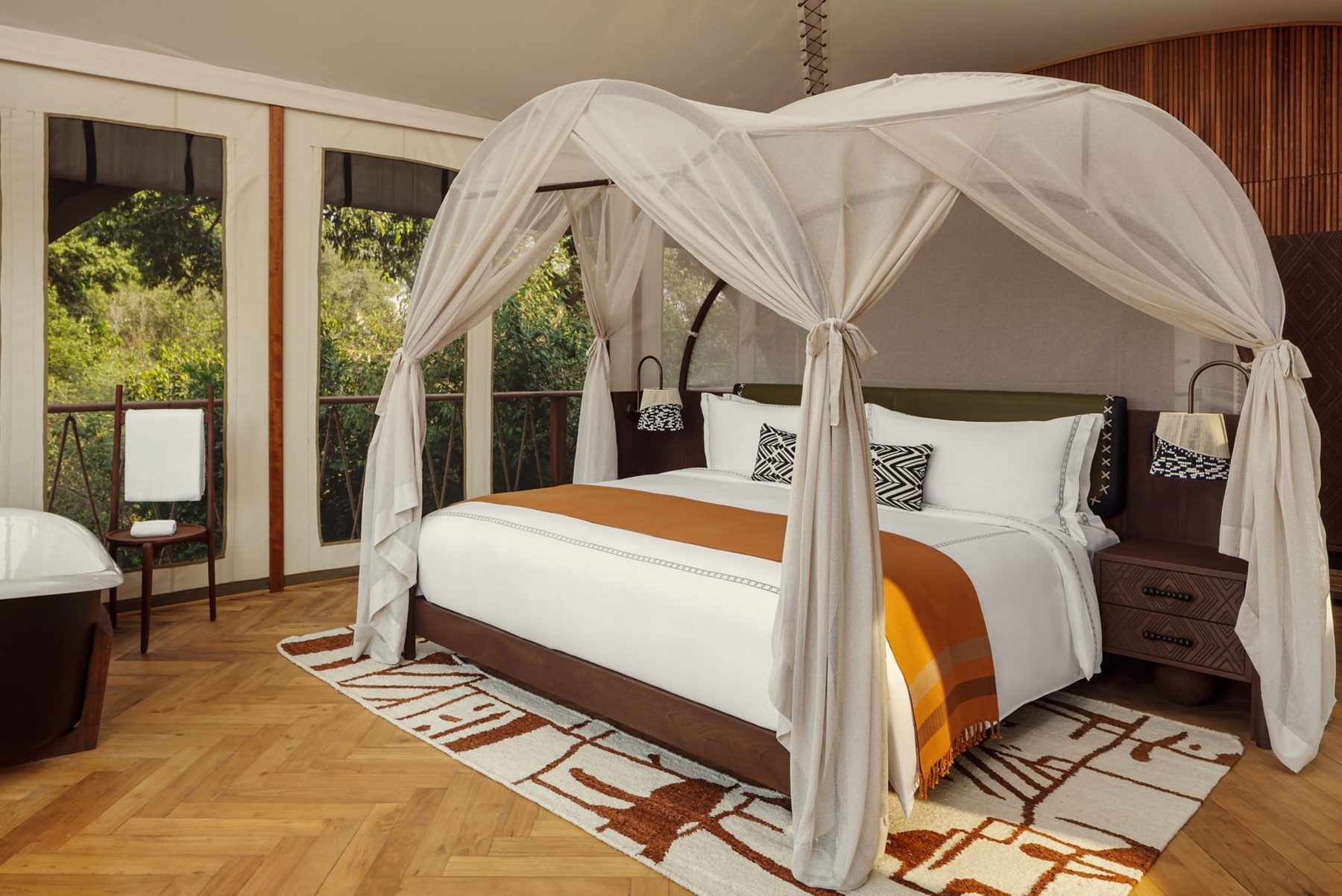Tented suite at The Ritz-Carlton, Masai Mara Safari Camp with a netted canopy bed, a patterned rug and views into the trees