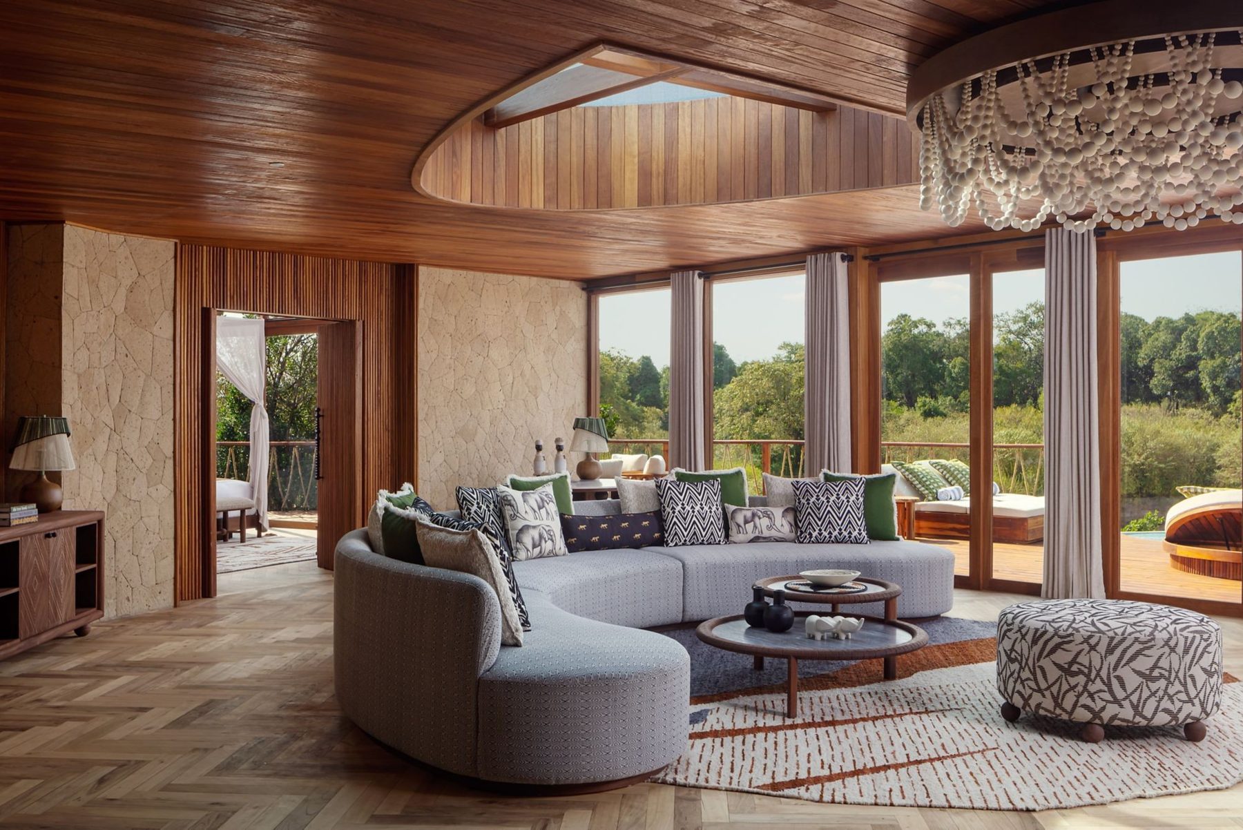 Suite sitting room at The Ritz-Carlton, Masai Mara Safari Camp with a curved grey sofa and tall windows onto the bush