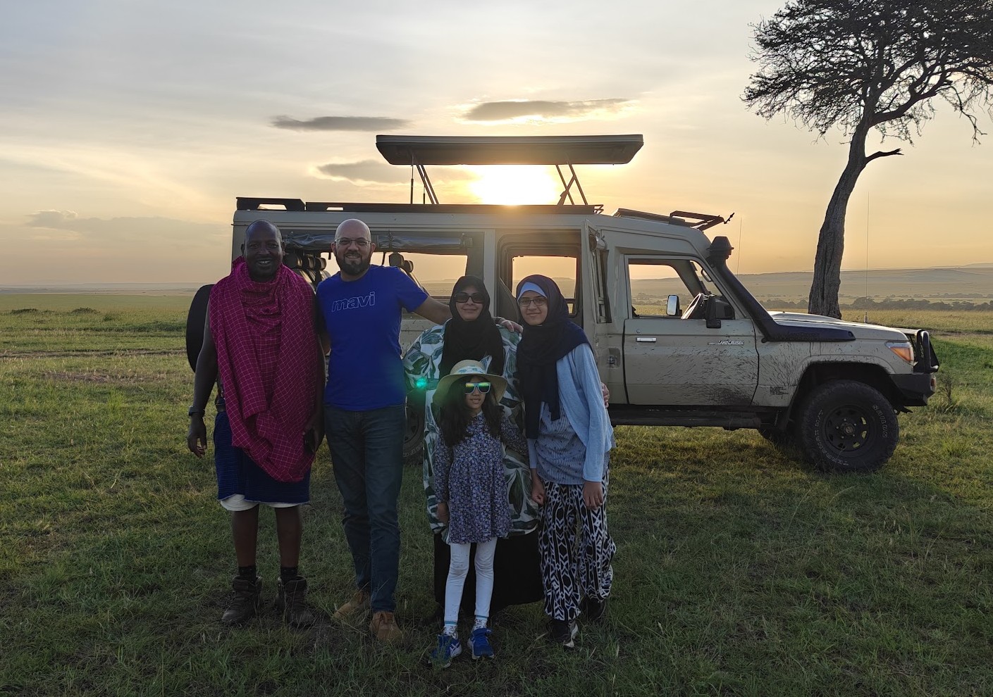 The Jagani family and their guide beside a safari vehicle at sunset in the Maasai Mara